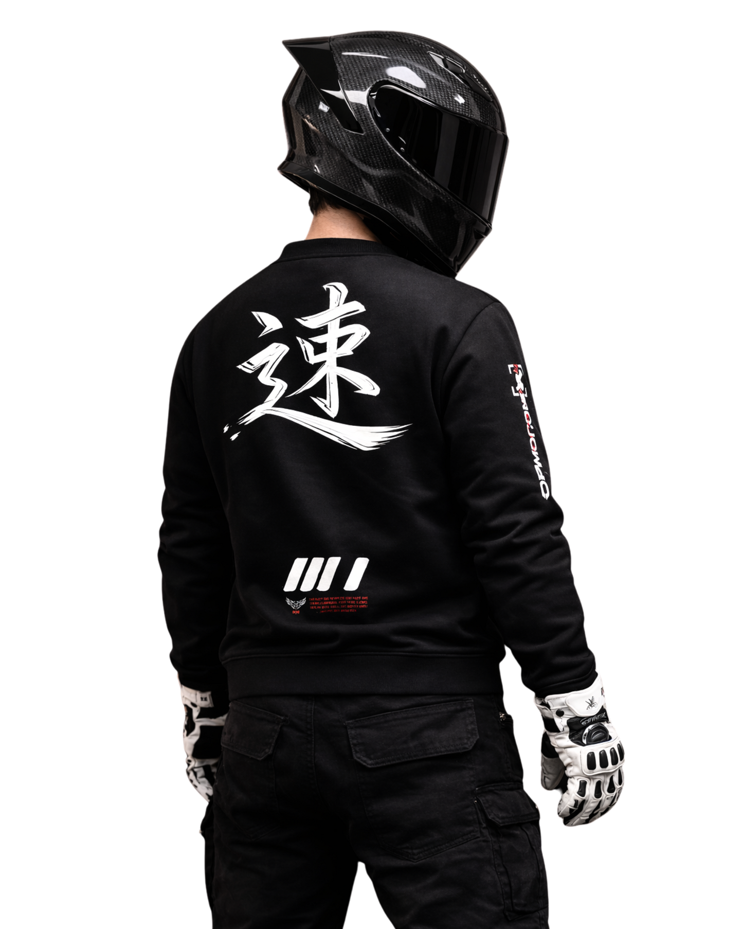 Motorcycle rider wearing black streetwear sweatshirt with bold back graphic and carbon full-face helmet, photographed from behind in dark studio, motorsport culture and speed-driven lifestyle.